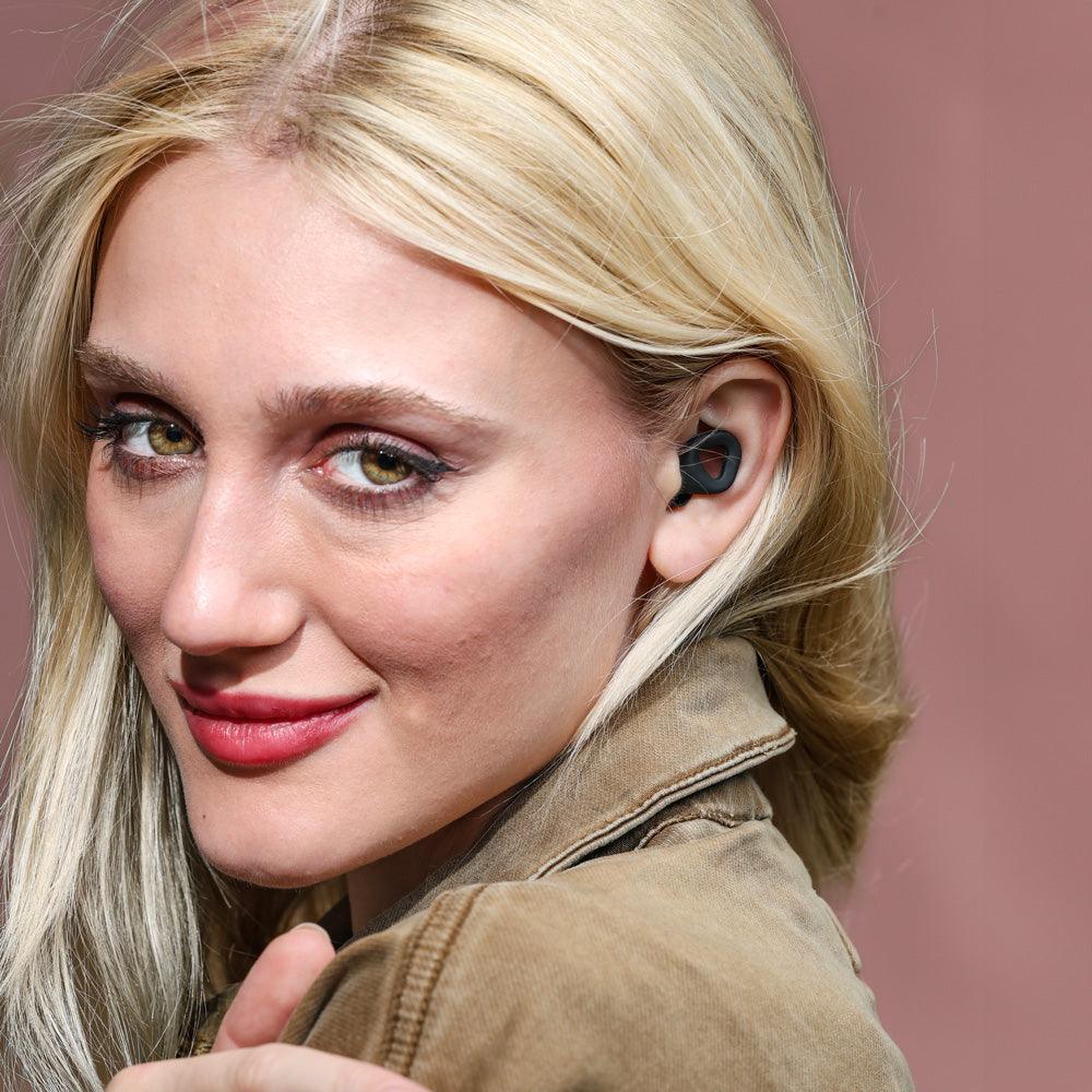 Woman wearing Zenz Unwind black earplugs, showcasing the stylish and comfortable fit for effective noise reduction.