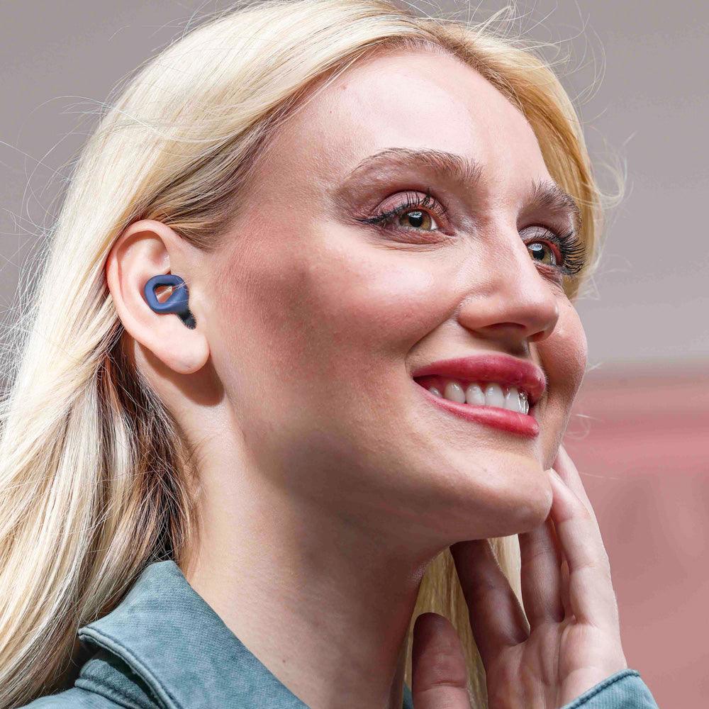 Woman wearing Zenz Unwind navy blue earplugs, emphasizing the stylish and comfortable fit for noise reduction.